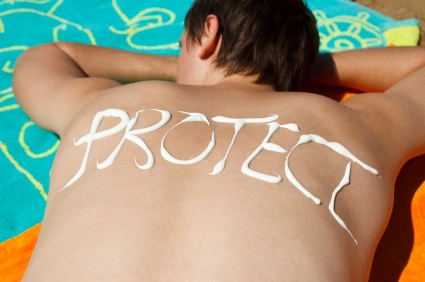 Man lying down at beach and protect written on his back with sunscreen.